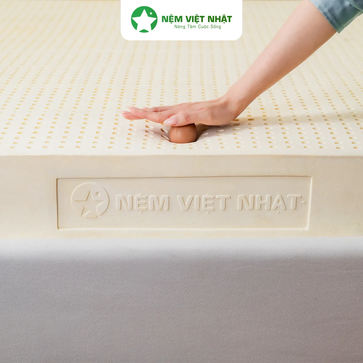 Bàn tay ấn quả trứng xuống mặt nệm cao su thiên nhiên Natural để test độ đàn hồi, trứng không vỡ
